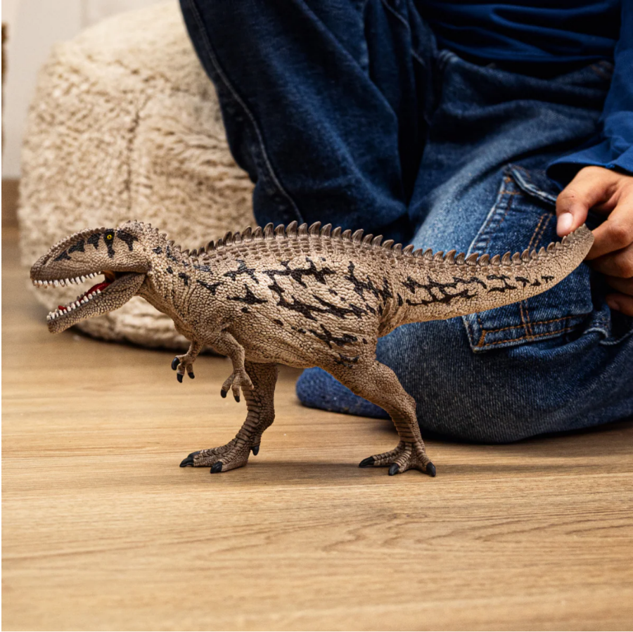 Toy dinosaur being held by a person on a wooden floor