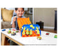 Excited boy in gray tshirt and end of orange plastic track, watches as hot wheels cars cross finish line. Finish line is the blue plastic end of track, with yellow number for each of the 5 tracks (1-5)--car flips up the number as it crosses the line. All on white table, scattered with Hot Wheels cars, 